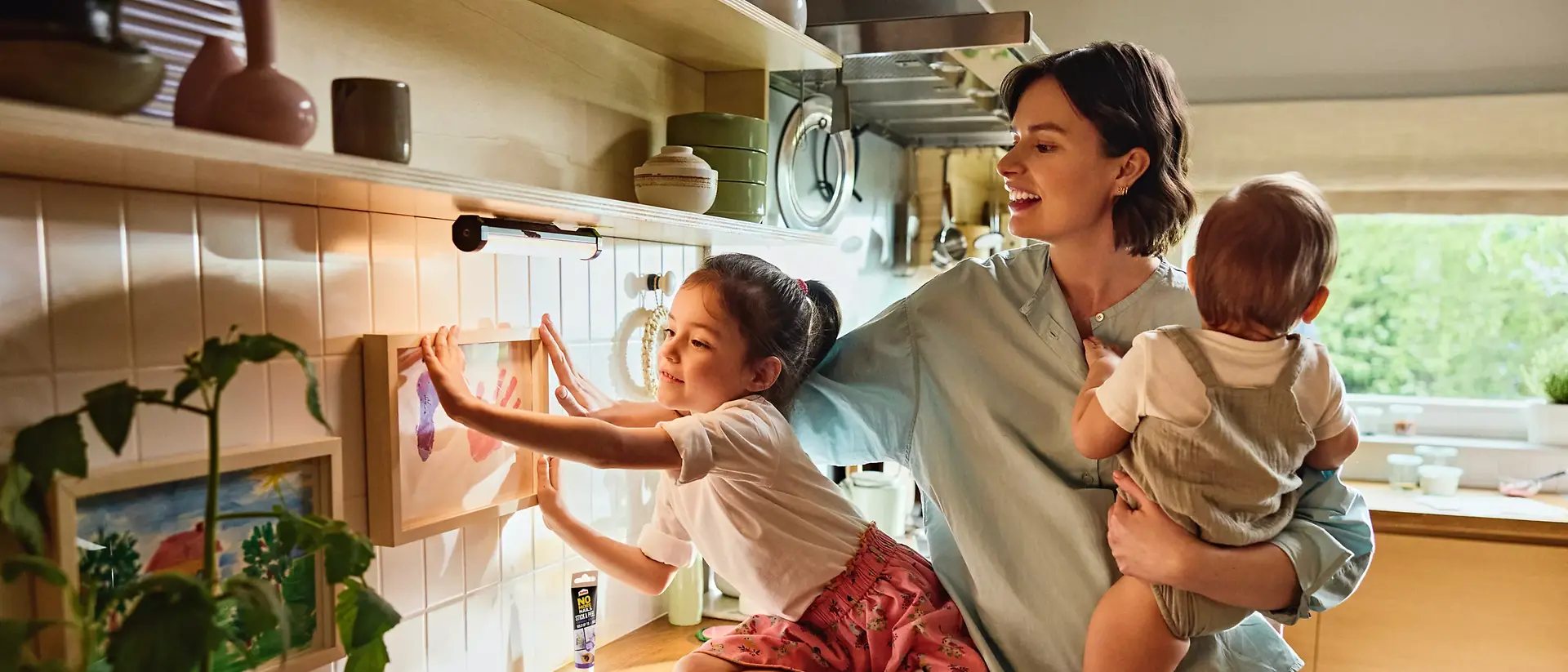 A mother and her daughters hang a picture on the wall using Pattex Stick and Peel.