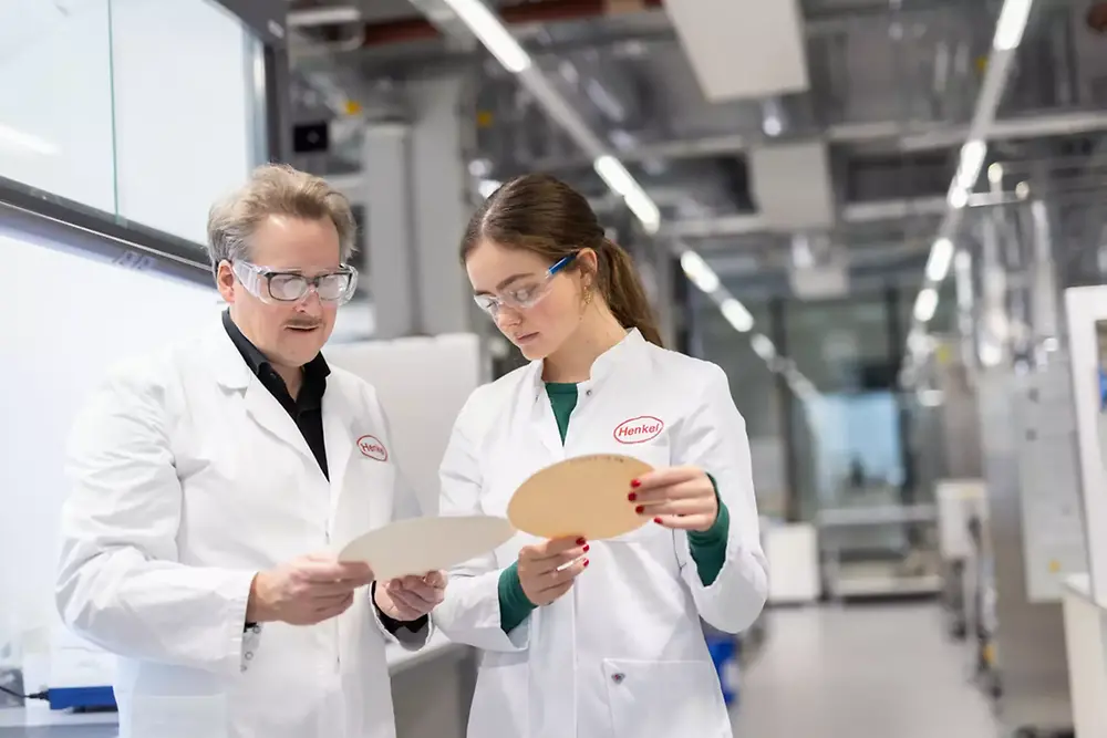 
A man and a woman in white Henkel lab coats examining circular samples.
