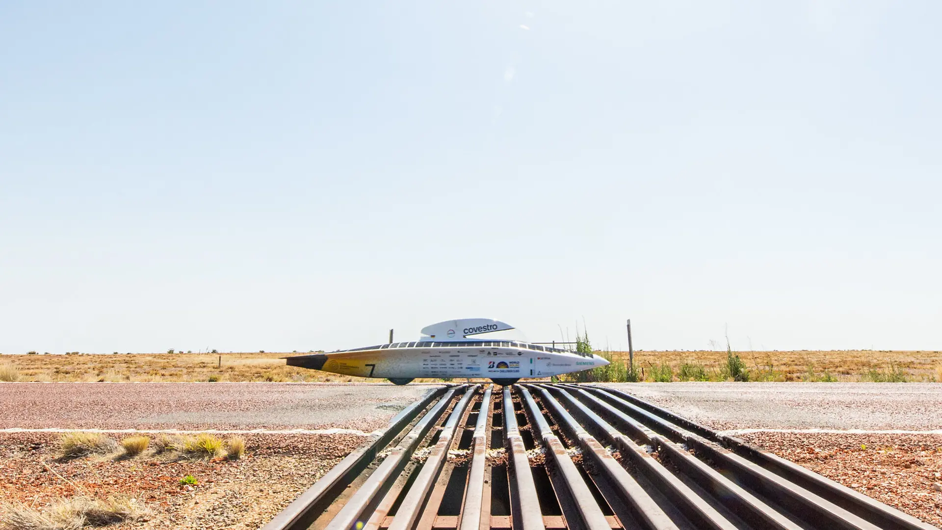 The solar car is driving on a road through a dry landscape. 